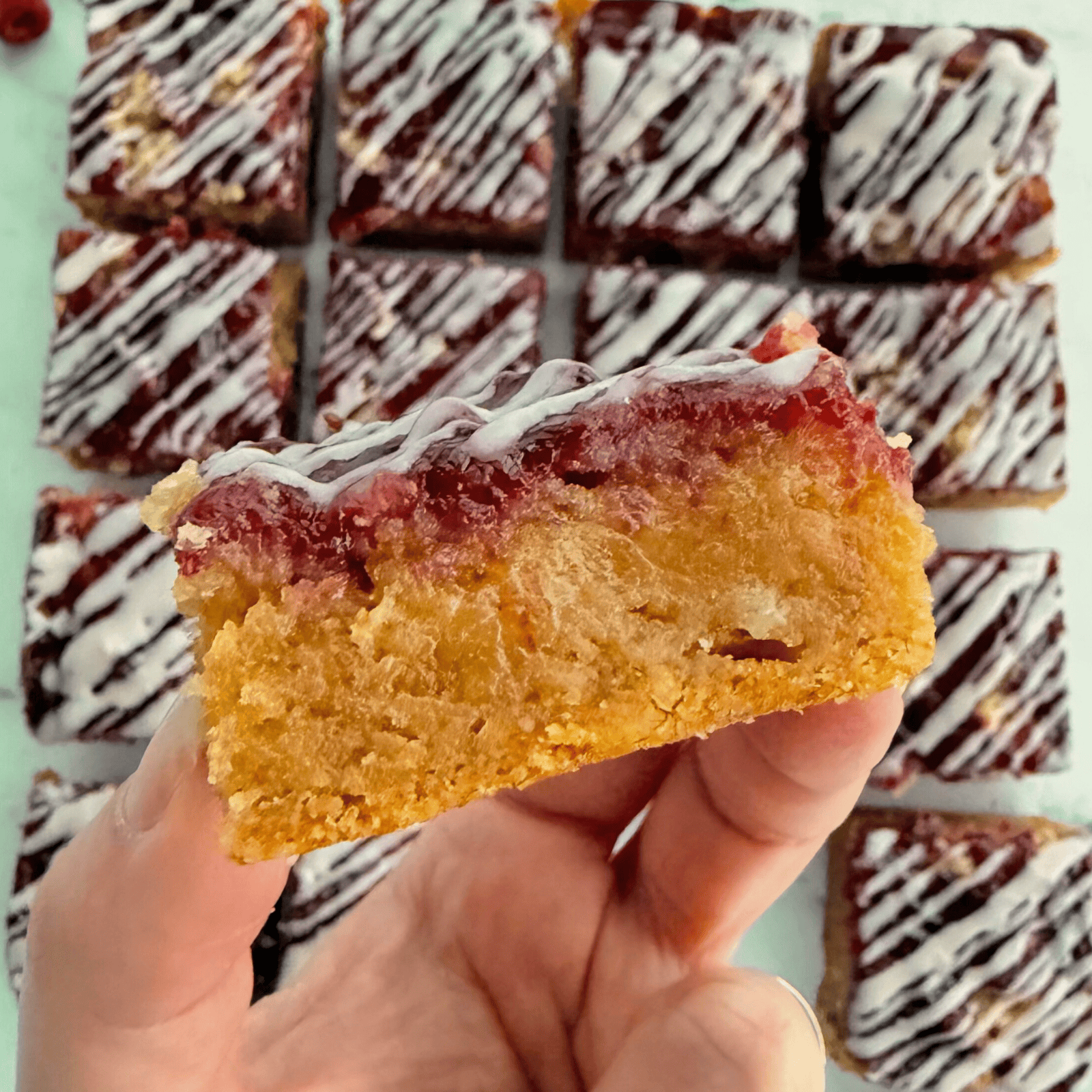 a hand holding a raspberry almond bar with the rest of the slices below.