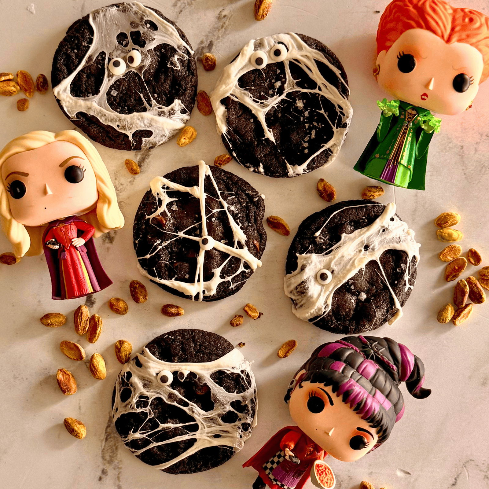 several hocus pocus cookies surrounded by pistachios and Funko Pop versions of the three witches from the movie.